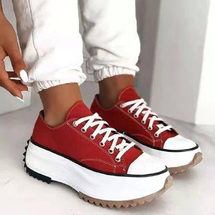 Red sneakers with white soles worn by a person on a light background