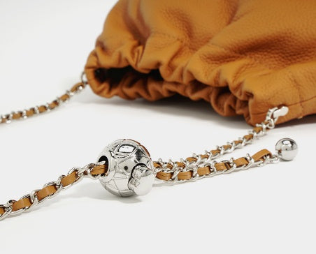 Silver charm with brown leather strap on a white surface with an orange fabric background