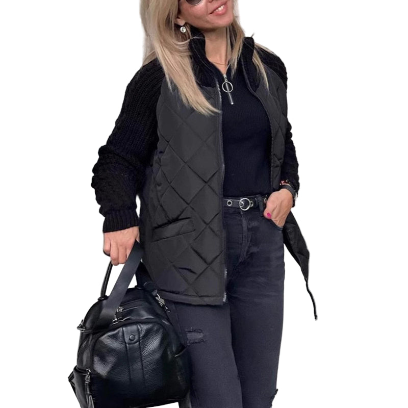 Woman wearing a black quilted vest and holding a black bag, standing in front of a white door.