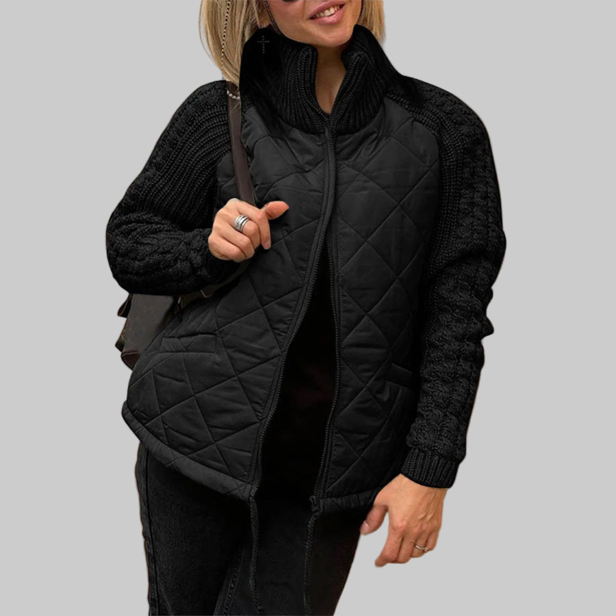 Person wearing a black quilted jacket against a beige wall