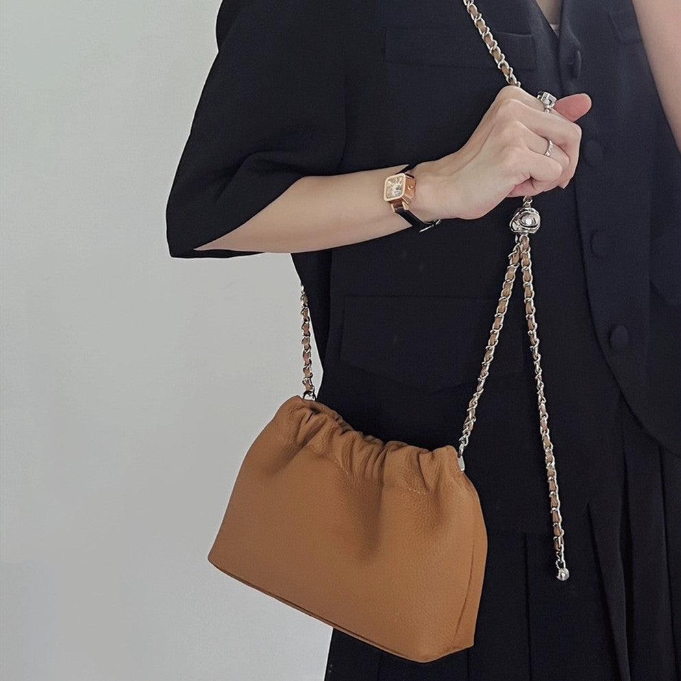 Person holding a brown handbag with a chain strap against a plain background