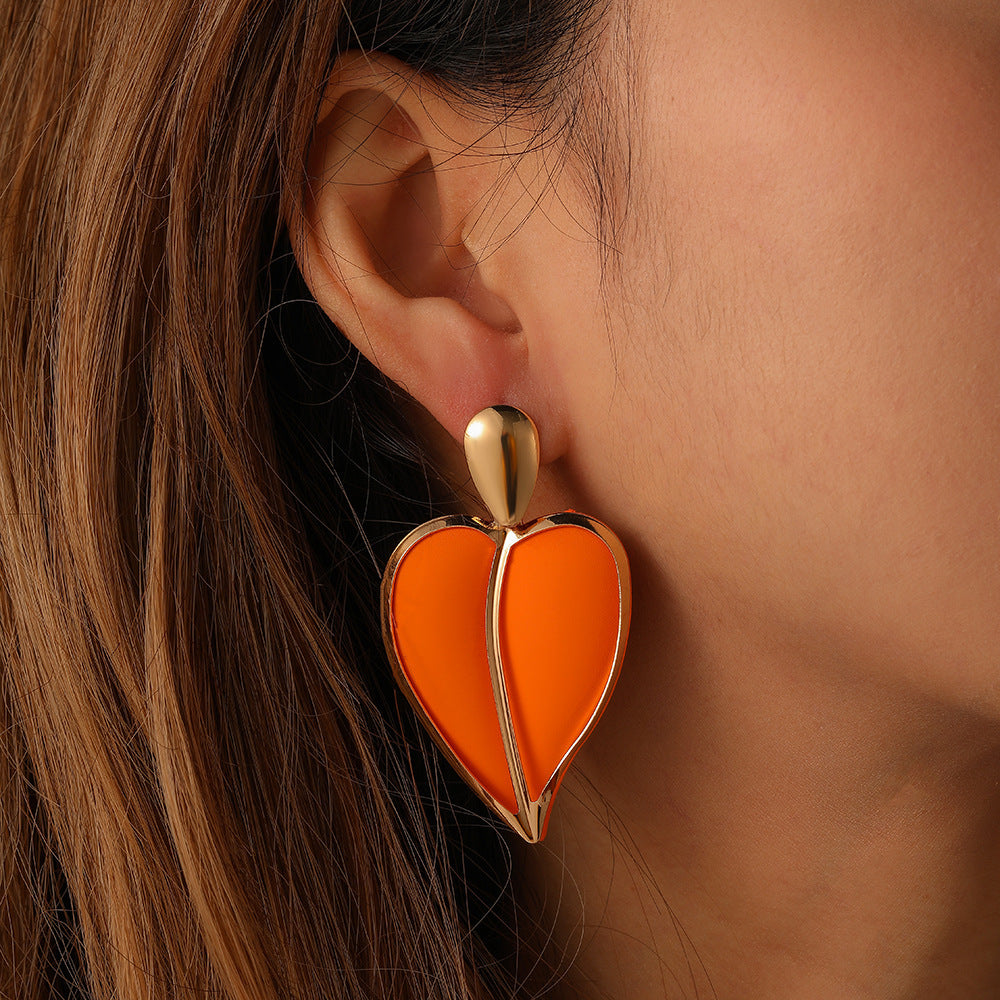 Orange heart-shaped earring worn by a person with brown hair.