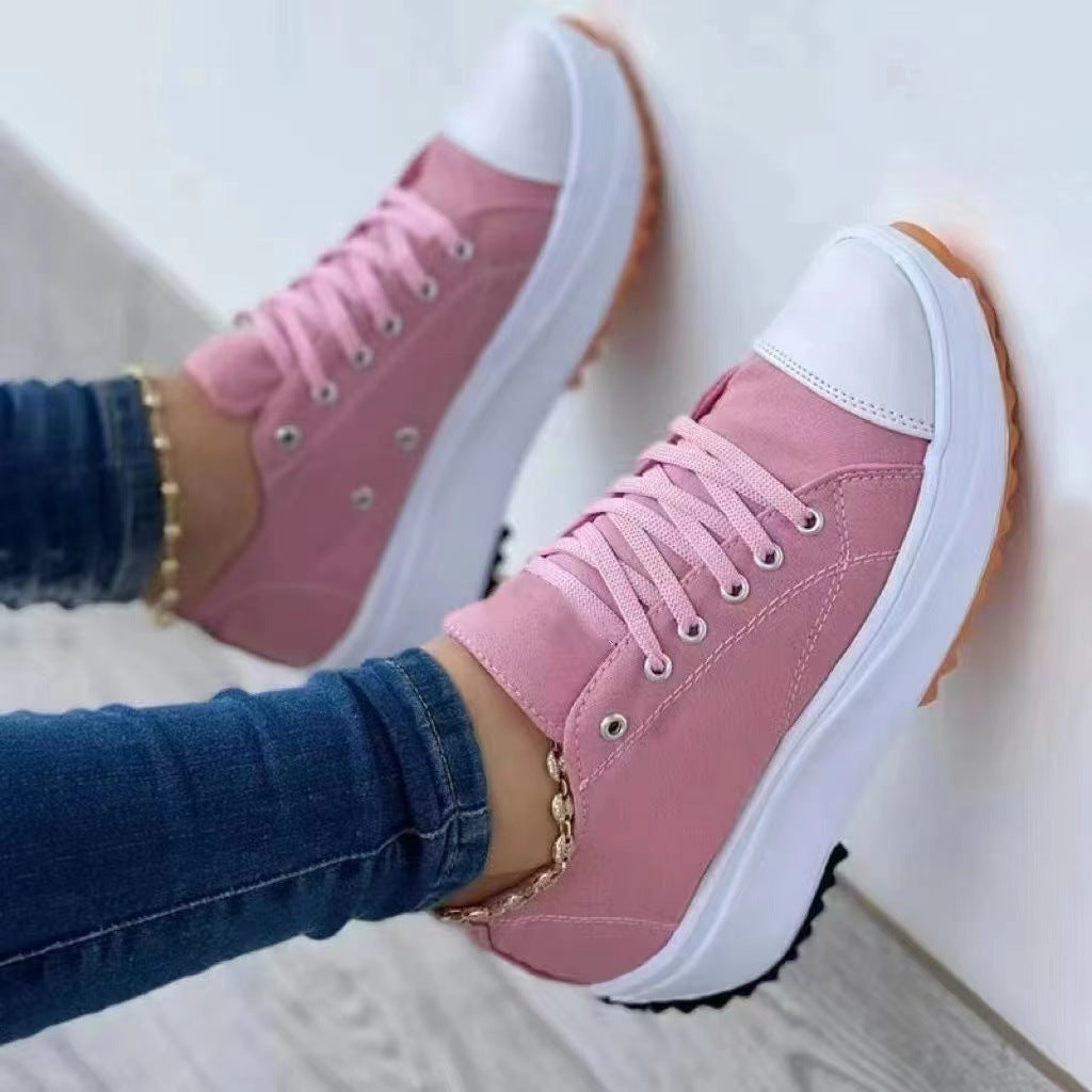 Pink sneakers with white soles worn by a person on a light wooden floor.