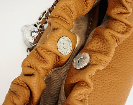 Close-up of a brown leather handbag with metal hardware on a white background