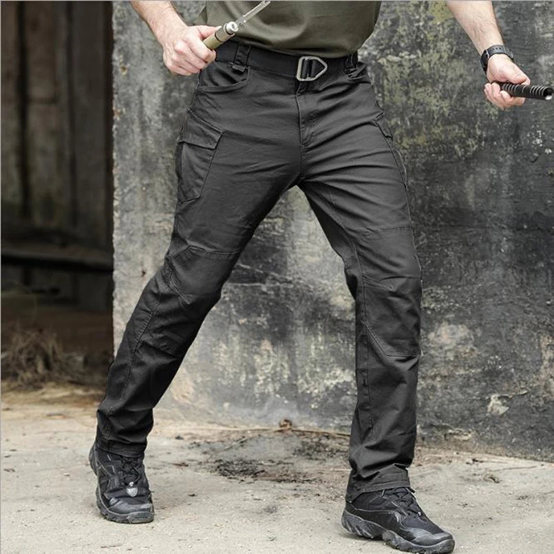 Person wearing black tactical pants with a belt, standing against a textured wall.
