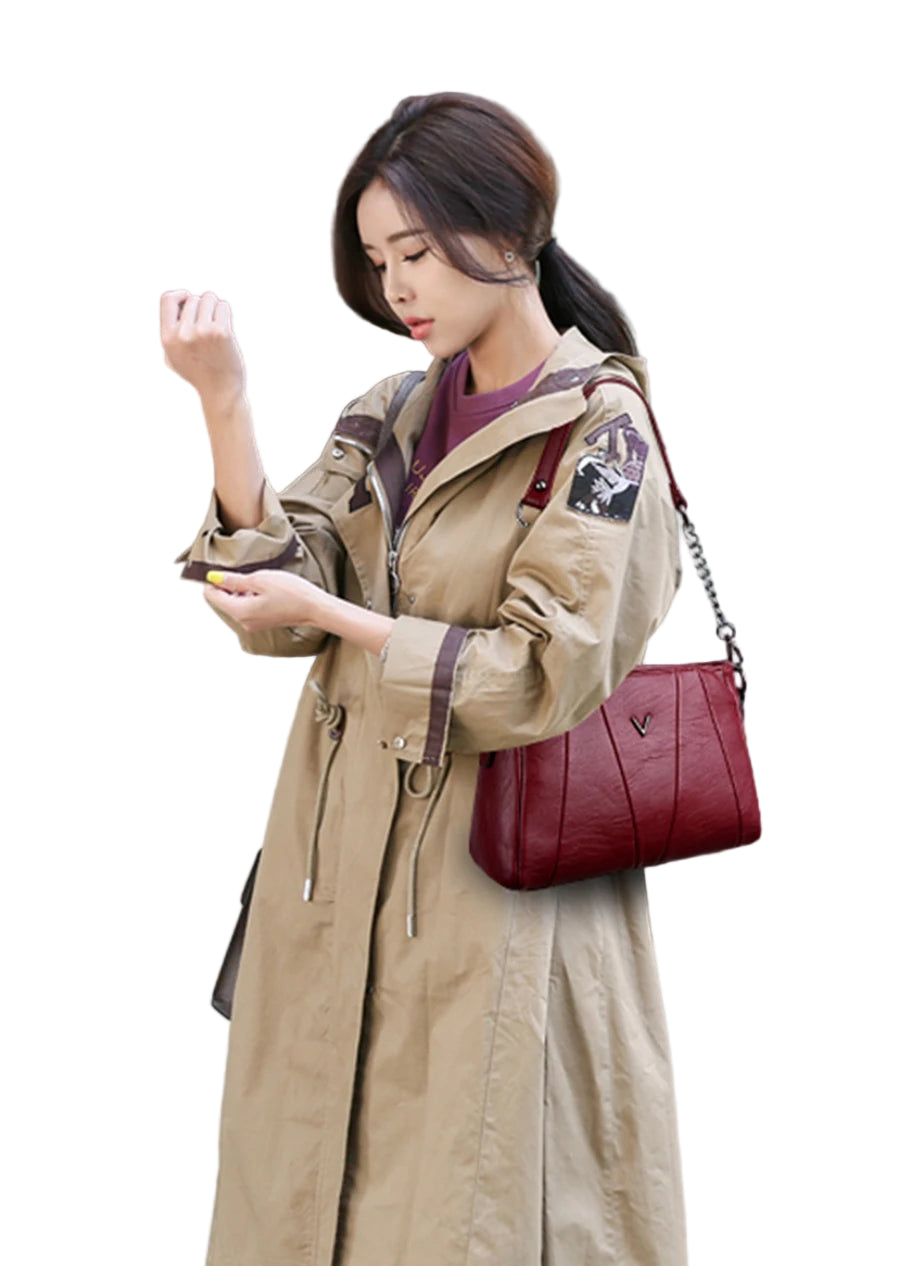 Woman in a beige trench coat holding a red handbag outdoors.