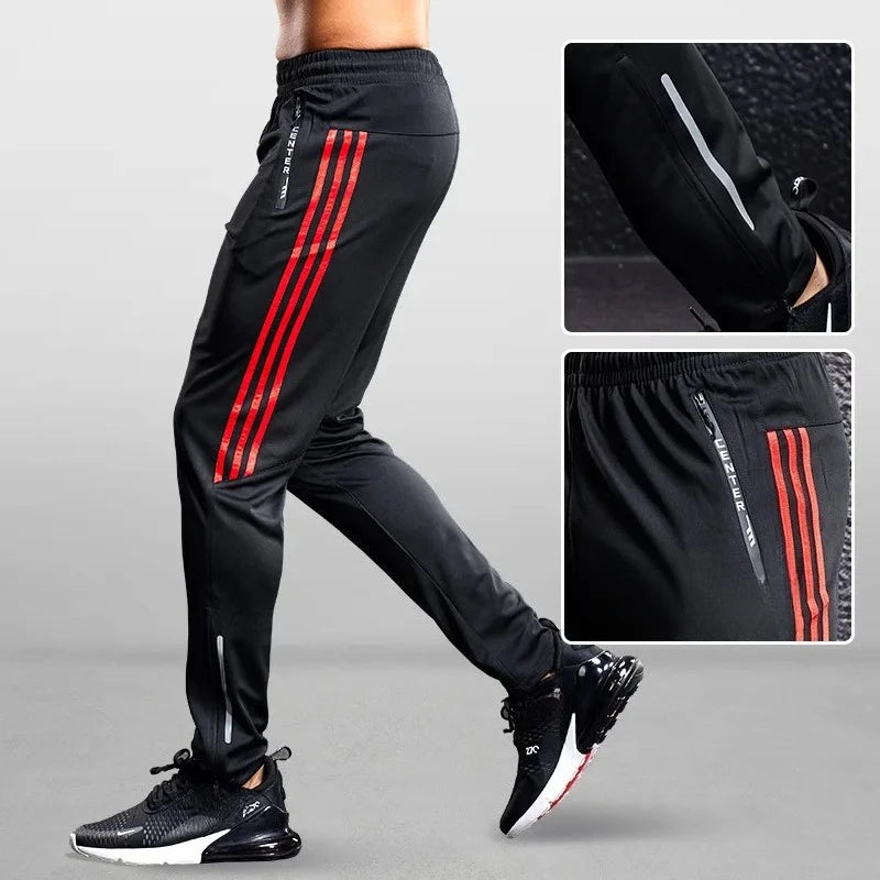 Black athletic pants with red stripes and black sneakers on a gray background