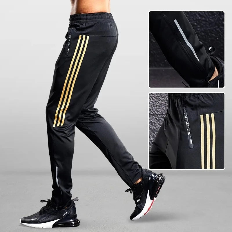 Black jogger pants with gold stripes worn by a person on a gray background