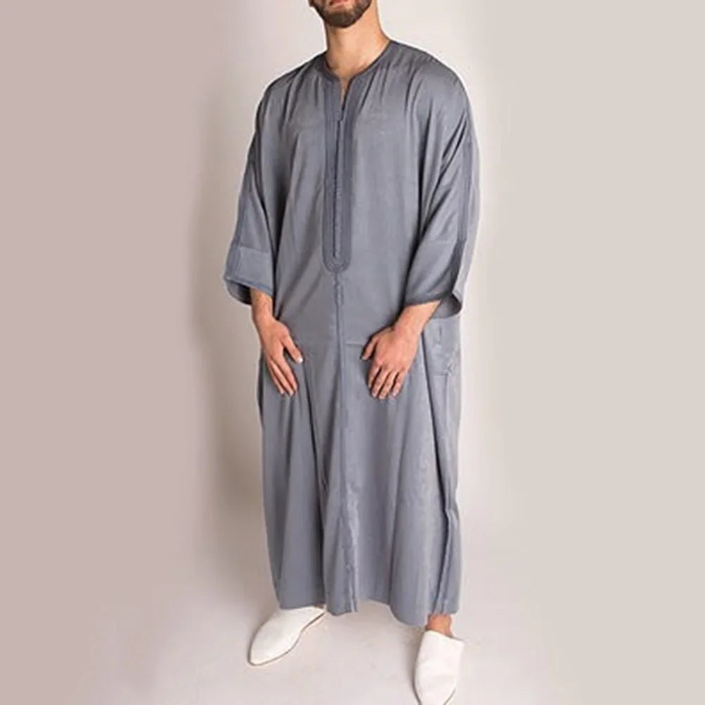 Man wearing a long gray garment against a plain background