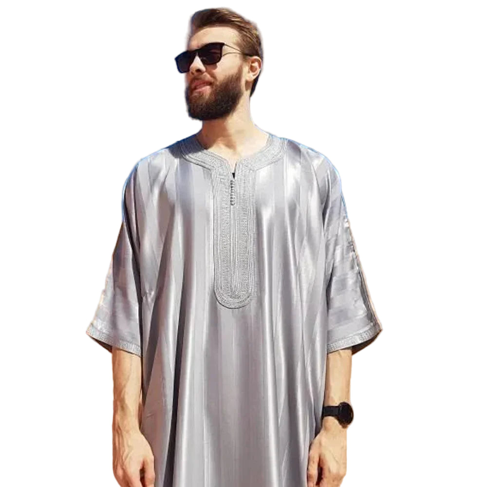 Man wearing a silver traditional outfit against a blue sky and sand dunes.