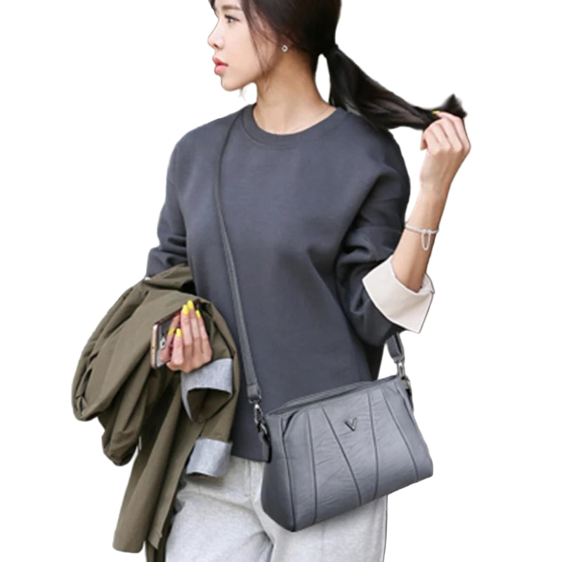 Woman holding a gray handbag and a jacket, standing outdoors.