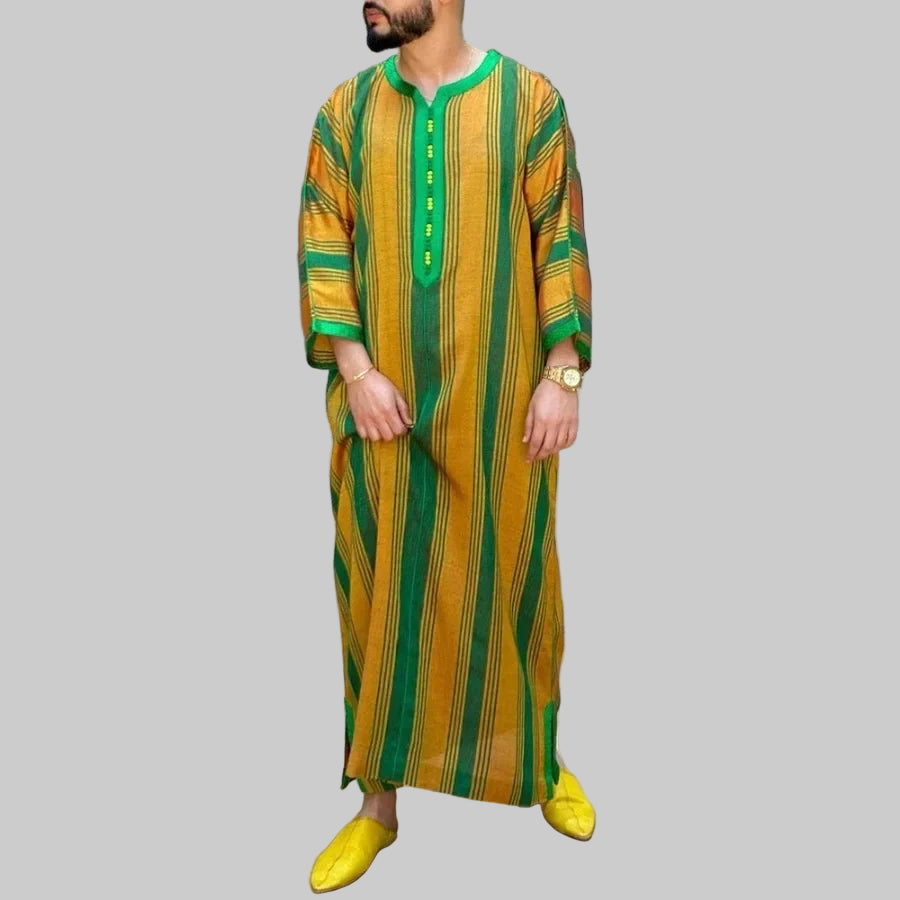 Man wearing a yellow and green striped outfit with yellow shoes, standing on a wooden deck with plants in the background.