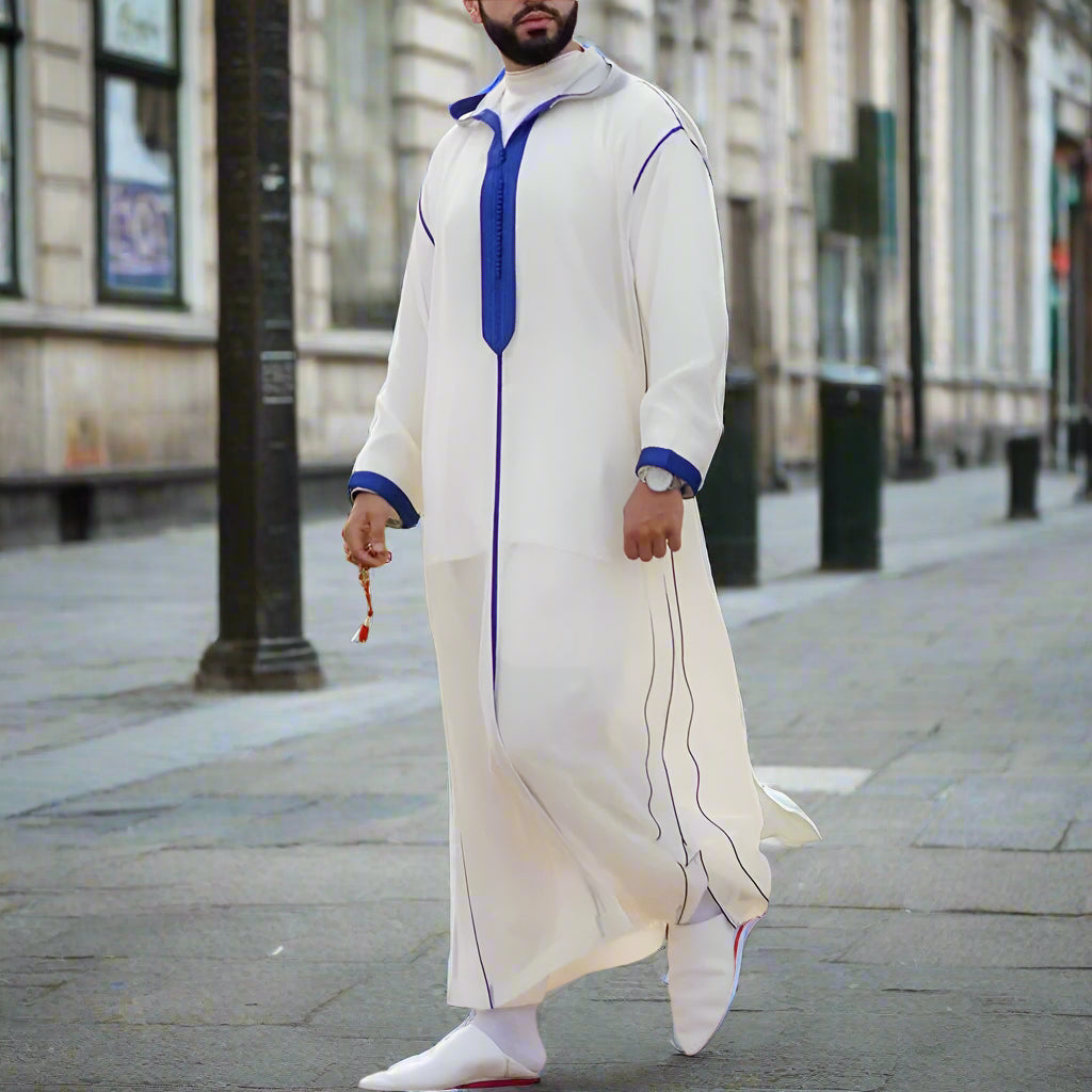 Person wearing a white and blue traditional outfit standing outdoors on a sunny day.