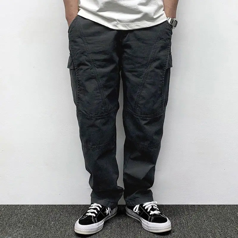 Person wearing black cargo pants and black sneakers against a white wall.