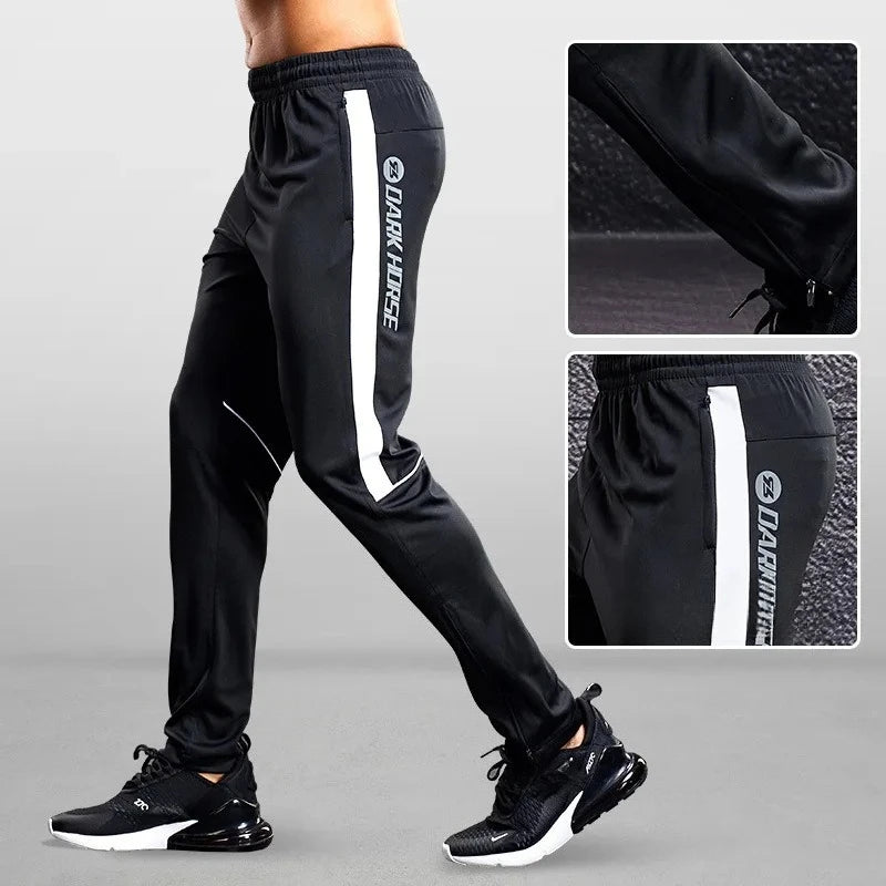 Black athletic pants with white stripes and brand logo on a gray background