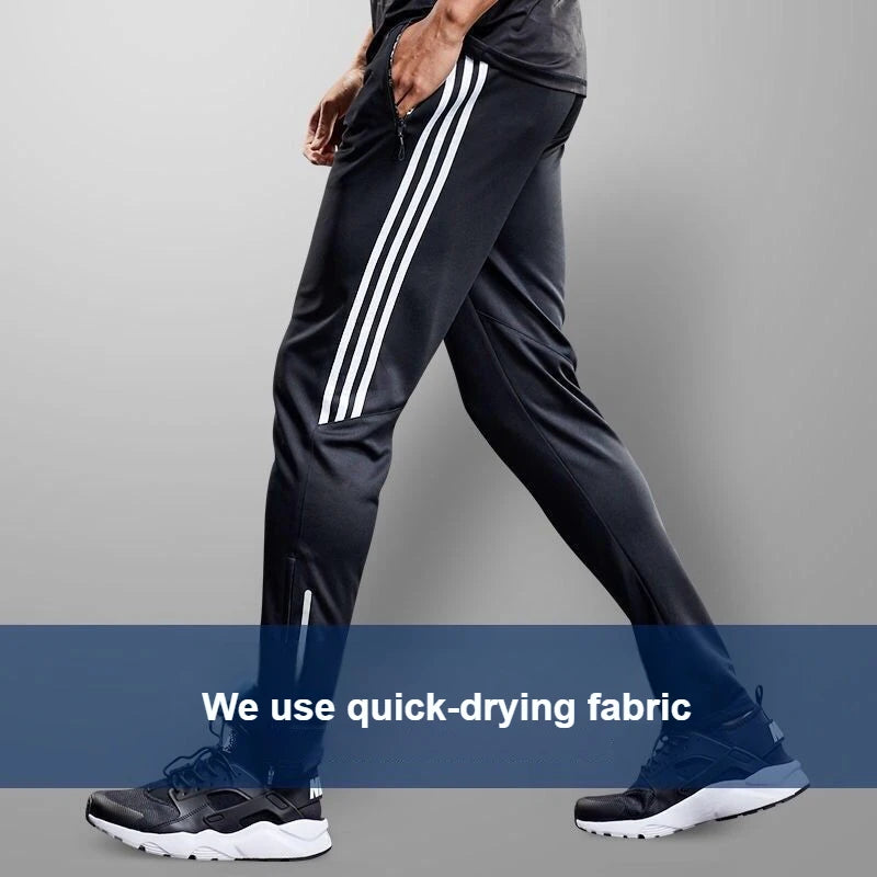 Person wearing black athletic pants with white stripes and dark sneakers on a gray background.