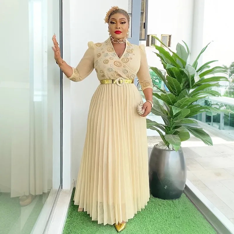 Woman in a beige dress standing in a modern interior setting with a plant.