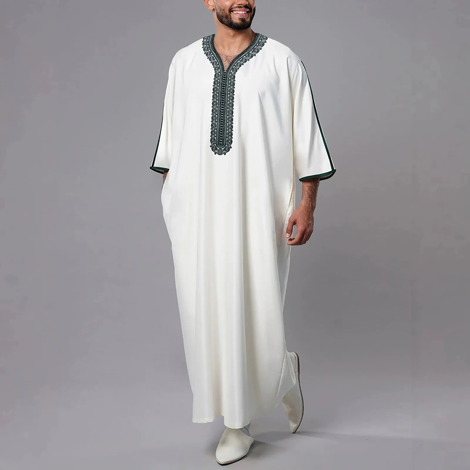 Man wearing a white robe with black embroidery on a gray background