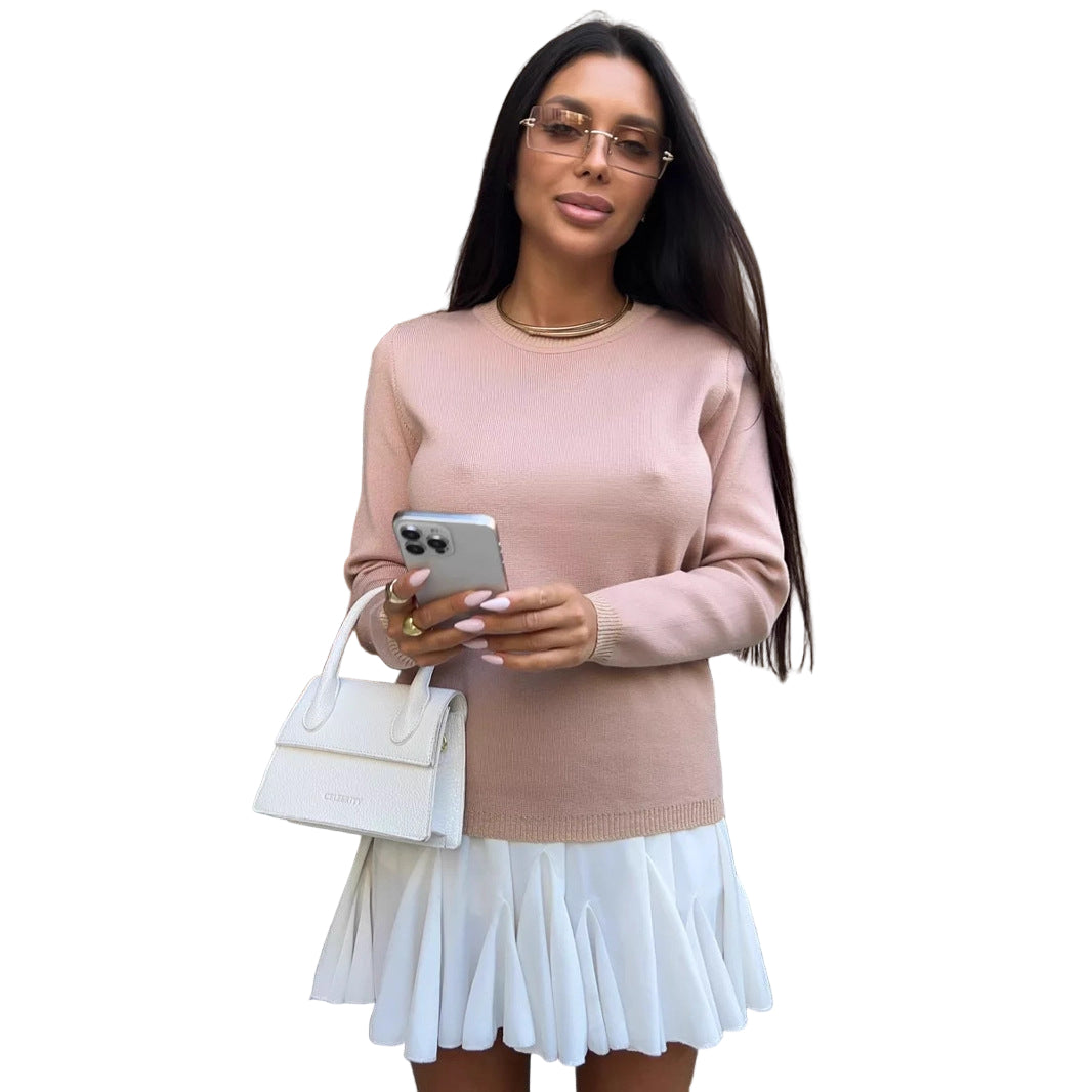 Woman in a pink sweater and white skirt holding a phone, standing on steps outside a building.